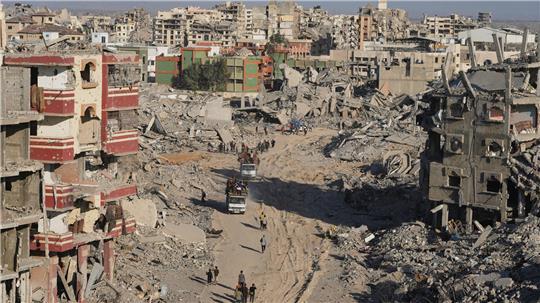 Vertriebene Palästinenser mit ihren Habseligkeiten gehen an zerstörten Gebäuden vorbei, während sie in ihre Häuser im Viertel Tal al-Hawa in Gaza zurückkehren.