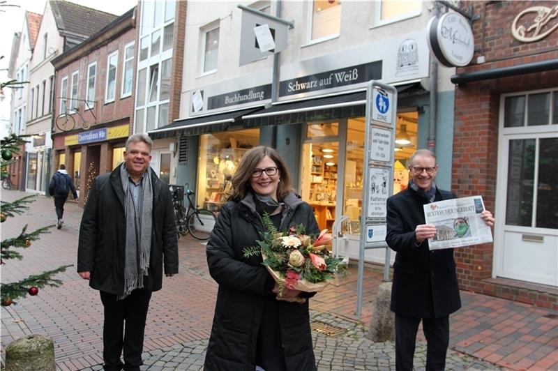 Vertriebsleiter Marcus Stenzel (links) und Geschäftsführer Georg Lempke (rechts) vom Zeitungsverlag Krause haben Blumen für Tanja Drecke mitgebracht: Ab 2. Januar wird die Buchhändlerin die neue TAGEBLATT-Agentur in ihrer Buchhandlung „Schw
