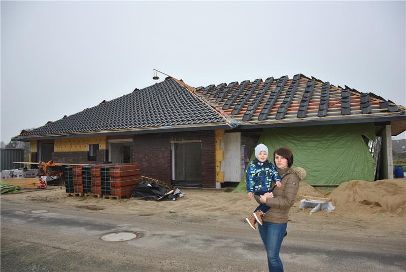 Verzweifelt wegen des Baustopps: Viktoria Fischer – mit Sohn Daniel (2) – vor ihrem halbfertigen Einfamilienhaus im Eulenweg im Baugebiet Nodorpsweg. Foto: Lohmann