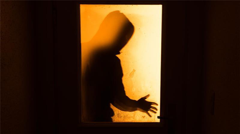 Der Schatten eines Mannes ist hinter einer gläsernen Wohnungstür zu sehen (gestellte Aufnahme).