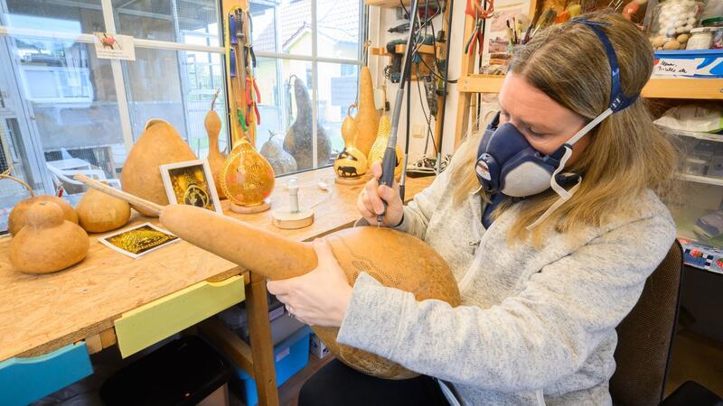 Virginia Lauterbach bearbeitet in ihrer Werkstatt einen Flaschenkürbis mit einem Bohrer.