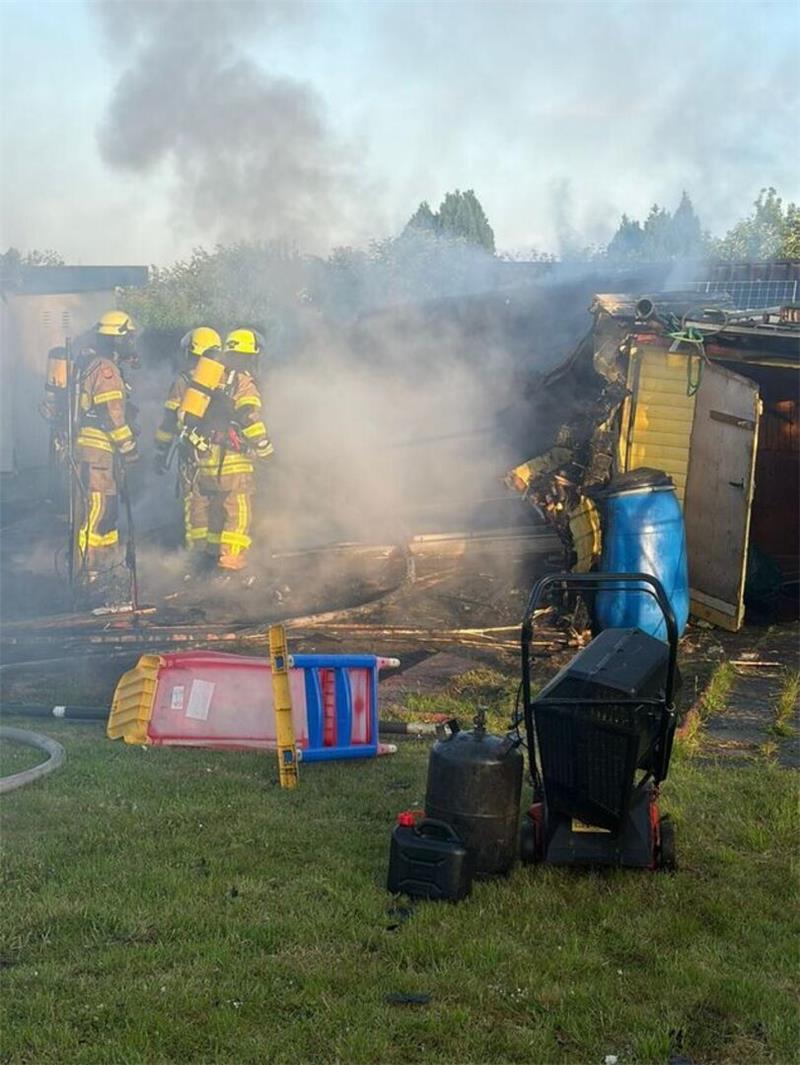 Vor der Gartenlaube steht ein Rasenmäher, eine Propangasflasche und ein Benzinkanister, die die Feuerwehr in Sicherheit gebracht hat.