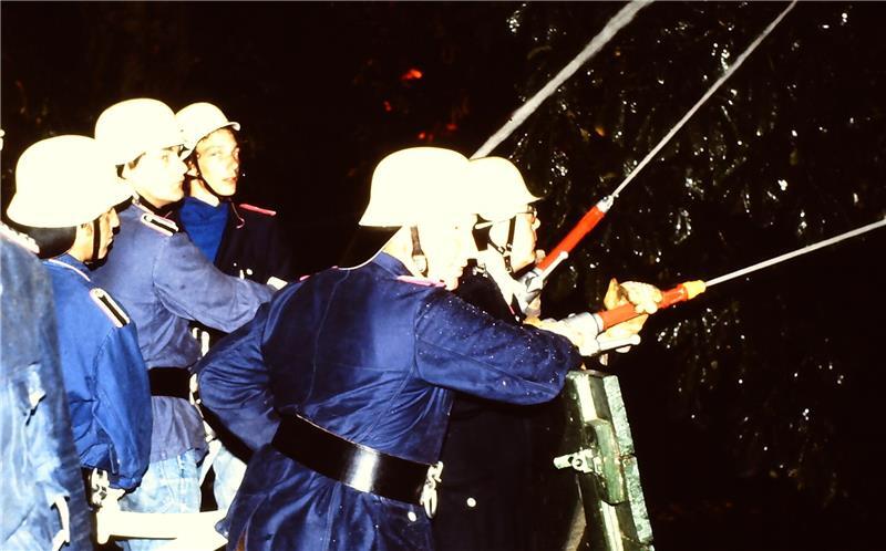 Vor der Hitze schützen sich die Feuerwehrleute beim Esteburg-Großfeuer von 1983 mit einer Holztür.