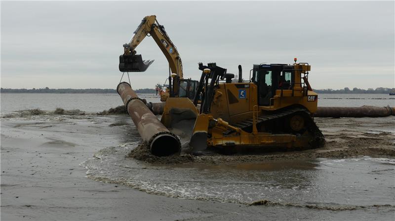 Während der Spülvorgang läuft, docken Baggerfahrer und Planierraupenfahrer in eingespieltem Teamwork ein weiteres Rohrstück an die Spülleitung an.