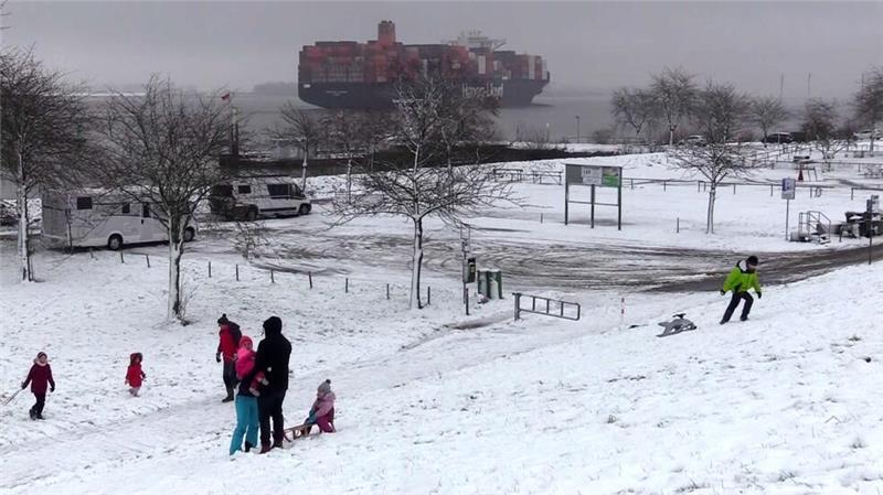 Während die Containerriesen den Lühe-Anleger passieren, nutzen Familien den Elbdeich zum Rodelspaß.