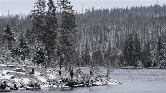 Wanderer gehen am leicht verschneiten Oderteich im Harz spazieren.