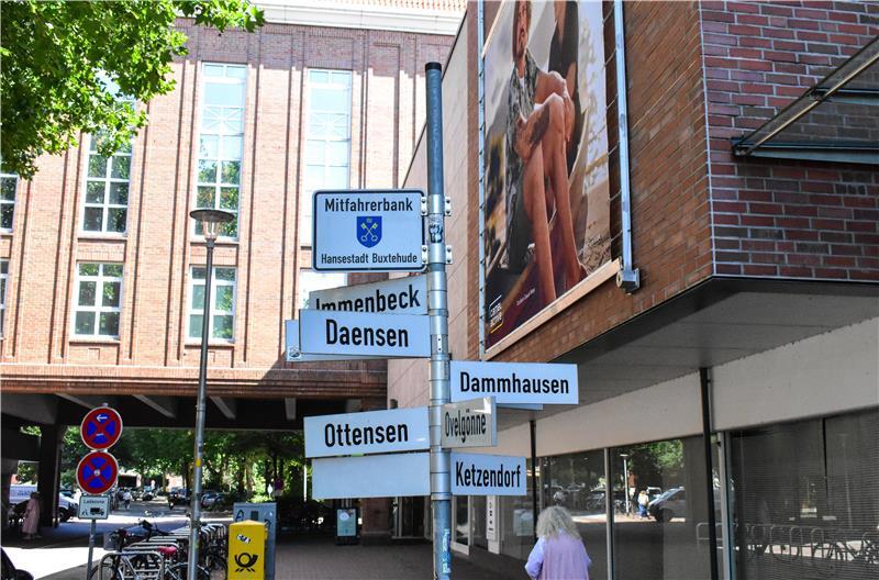 Hollywoodreif: Mit ChatGPT auf Entdeckungsreise durch Buxtehude Wegweiser und Mitfahrerbank vor dem Modehaus Stackmann.