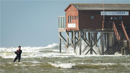 Wellen peitschen an die Pfähle eines Restaurants am Strand von St. Peter Ording. (Archivbild) Foto: Jonas Walzberg/dpa