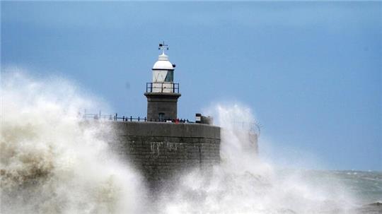 Wellen schlagen vor dem Leuchtturm an die Hafenmauer in Folkstone.