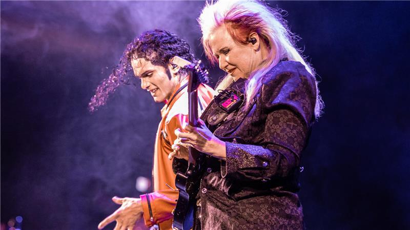 Hommage an Michael Jackson: Tribute-Konzert für den „King of Pop“ Wendel Gama als Michael Jackson in orangefarbener Lederjacke neben Original-Gitarristin Jennifer Batten an der Bass-Gitarre in „One Night of MJ“.