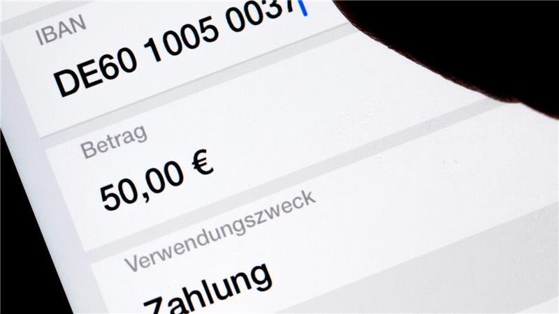 Eine Frau nutzt auf ihrem Smartphone eine App, um im Online-Banking eine SEPA-Überweisung zu veranlassen (gestellte Szene). 