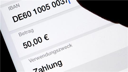 Eine Frau nutzt auf ihrem Smartphone eine App, um im Online-Banking eine SEPA-Überweisung zu veranlassen (gestellte Szene). 