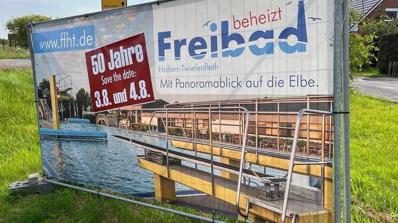 Werbebanner für das Freibad-Jubiläum stehen an den Straßen der Gemeinde.