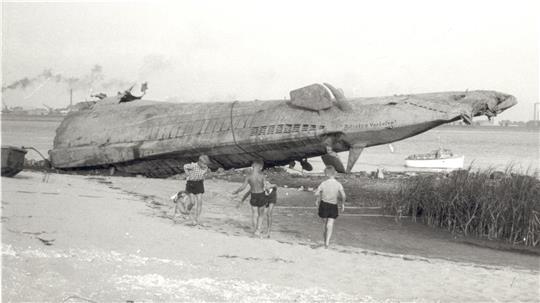 Wie ein abgestürztes Raumschiff liegt es am Strand von Blexen: Das Heck eines deutschen U-Bootes - 1945 von der Besatzung selbst in der Außenweser versenkt, einige Jahre später von mutigen Männern des Schrottwerts wegen wieder geborgen. Kinder spielen davor - ein Bild, in dem sich die 50er Jahre des Nachkriegsdeutschlands verdichten. Bei dem Boot dürfte es sich um U 38, ein Boot vom Typ IX A, gehandelt haben - 1938 in Dienst gestellt und 1.032 Tonnen schwer. Foto: Fritz Frerichs, Archiv des RHB