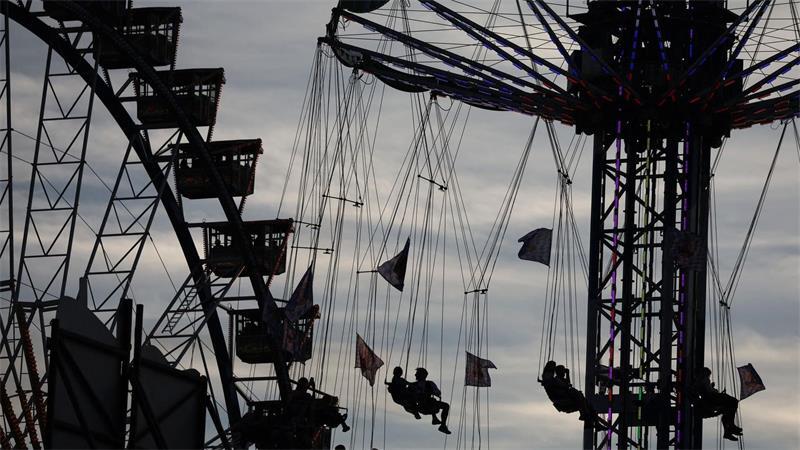 Wiesn-Besucher sitzen am Abend in einem Karussell vor dem Riesenrad auf dem Oktoberfest.