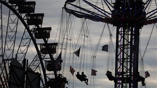 Wiesn-Besucher sitzen am Abend in einem Karussell vor dem Riesenrad auf dem Oktoberfest.