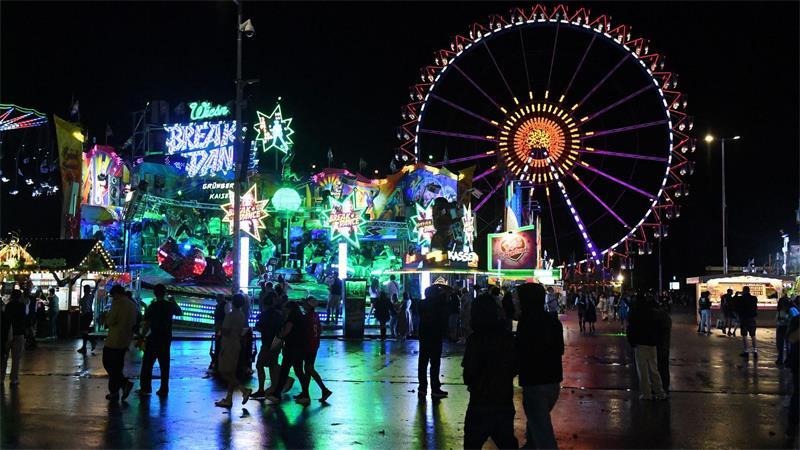Wiesnbesucher gehen bei Regen über das Oktoberfest. 