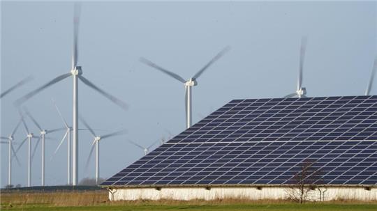 Windenergieanlagen stehen neben einer Halle mit Photovoltaik-Anlagen auf dem Dach.