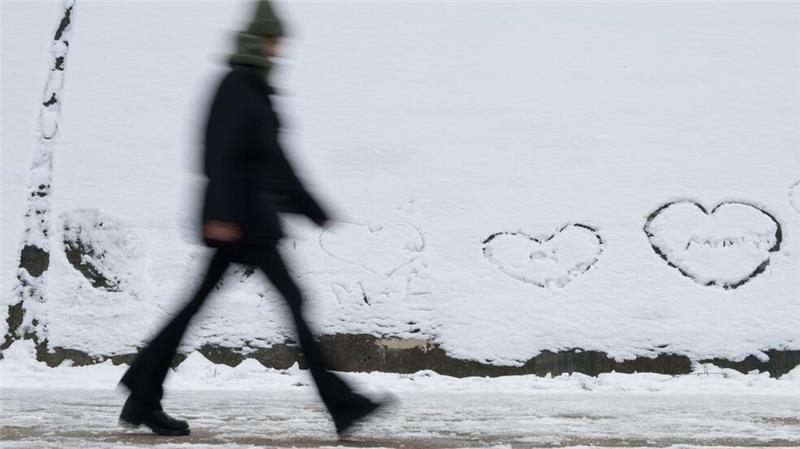 Winterwetter in Berlin: Eine Person geht an einer Wand vorbei, auf der im Schnee Herzen geschrieben sind.