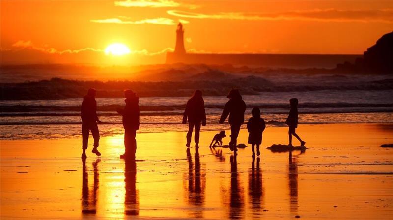 Winterwetter in Großbritannien: Spaziergänger gehen bei Sonnenaufgang am Strand von Tynemouth