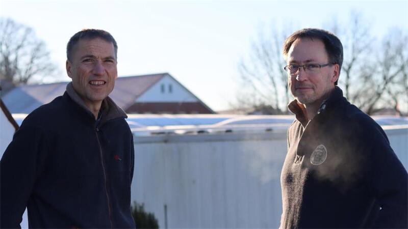 Wolf und Peter Warncke stehen auf dem Dach eines Gebäudes auf ihrem Betriebsgelände. Im Hintergrund sind die neuen Solarmodule auf dem Dach der Neuwagenhalle zu sehen.