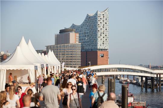 Zahlreiche Menschen genießen auf der Jan- Fedder-Promenade am Hafen die Abendsonne.