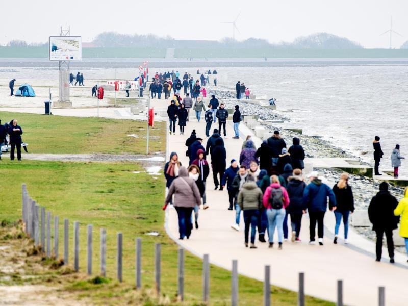 Zahlreiche Spaziergänger sind bei trübem Wetter auf einer Promenade am Strand unterwegs. Foto: Hauke-Christian Dittrich/dpa