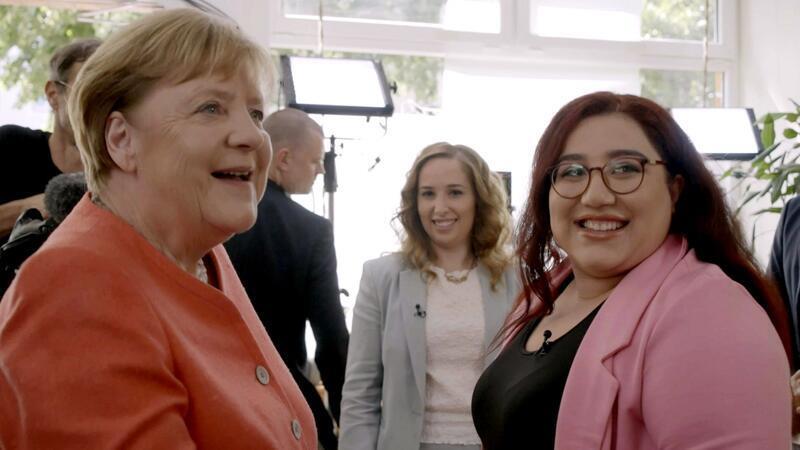 Zehn Jahre nach ihrem Versprechen „Wir schaffen das“ trifft Angela Merkel die heute 27-jährige Mahsa Narimani (rechts), ihren Mann und andere Geflüchtete in einem Restaurant in Berlin.