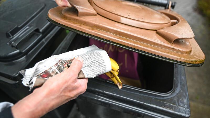 Eine Banane wird in Zeitungspapier eingewickelt in den Biomüll geworfen.