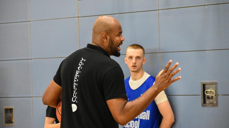 NBA-Camp in Stade: Junge Basketballer lernen von den Profis Paulo Prestes erklärt Spielern etwas und zeigt mit seiner rechte Hand vier Finger.
