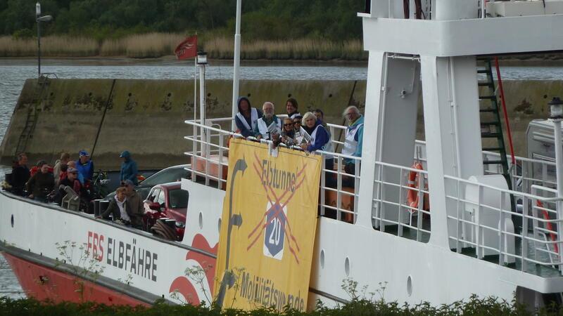 Elbfähre Glückstadt-Wischhafen: „Situation wird immer schlimmer“ Zum Tag der Mobilitätswende hatten die A20-Gegner ein Banner außenbords der Elbfähre befestigt. Die Fährverbindung über die Elbe müsse ausgebaut werden, fordern sie.