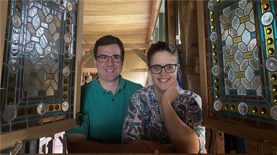 Jan und Sophia Sand schauen durch ein altes Kirchenfenster, das als Schmuckelement zwischen Eingangs- und Wohnbereich eingebaut wurde. 