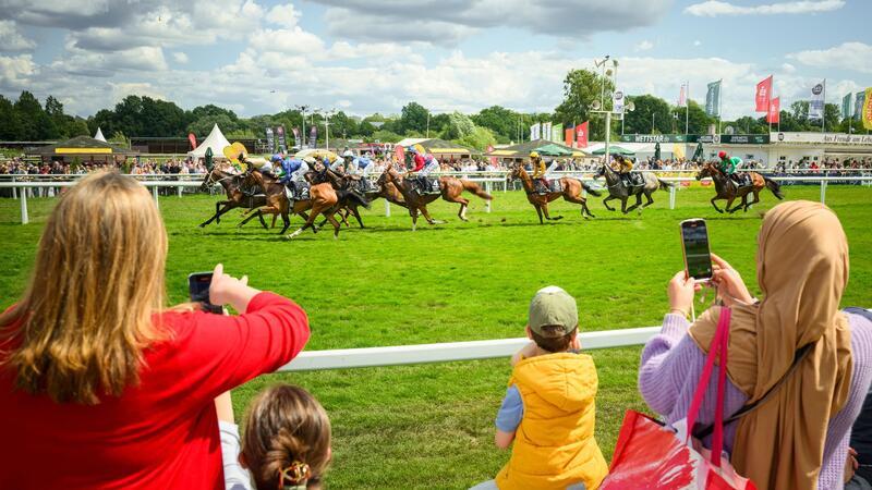 Zuschauende beobachten und fotografieren vom Rand der Bahn den Start der Pferde.