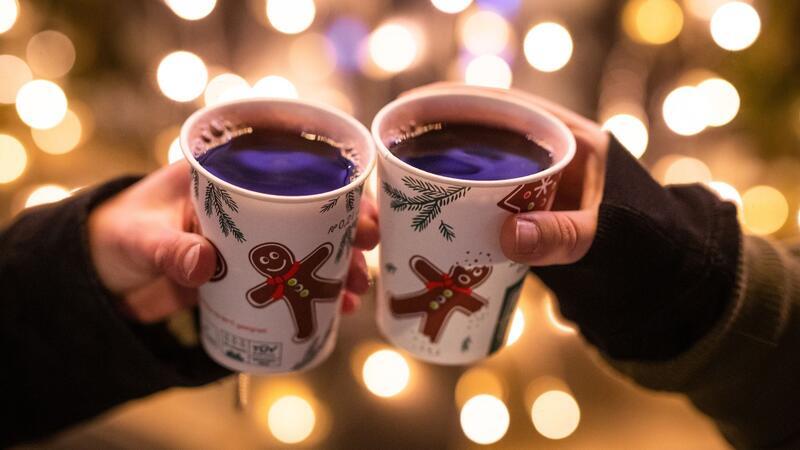 Zwei Besucherinnen eines Weihnachtsmarktes stoßen mit Glühwein an.