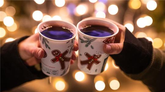 Zwei Besucherinnen eines Weihnachtsmarktes stoßen mit Glühwein an.