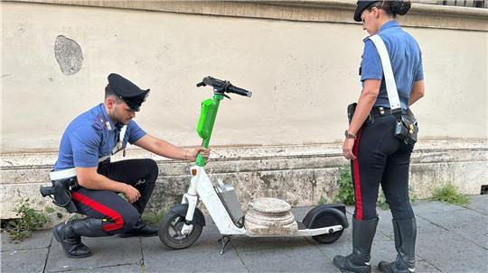 Zwei Carabinieri begutachten den Marmorsockel auf einem elektrischen Leihroller.