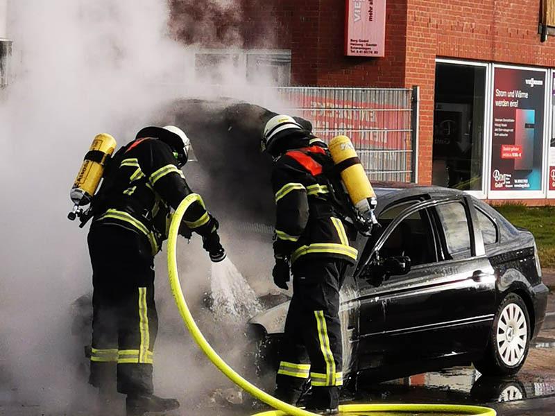Zwei Feuerwehrleute löschen den brennenden BMW. Das Fahrzeug war während der Fahrt in Brand geraten. Foto: Polizei