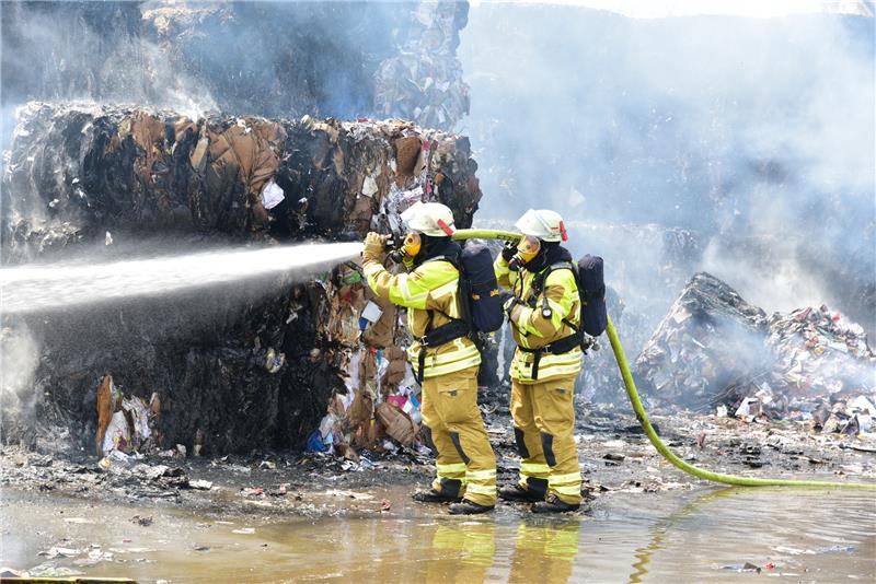 Großfeuer im Stader Recyclingzentrum unter Kontrolle Zwei Feuerwehrleute löschen die in Brand geratenen Pressballen in dem Recyclingzentrum. Foto: Beneke