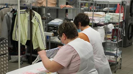 Zwei Frauen arbeiten in der Wäscherei der Lebenshilfe Gera e.V und legen dort Wäsche zusammen.