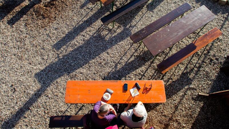 Zwei Frauen sitzen bei sonnigem Wetter an einem Biertisch in einem Biergarten.