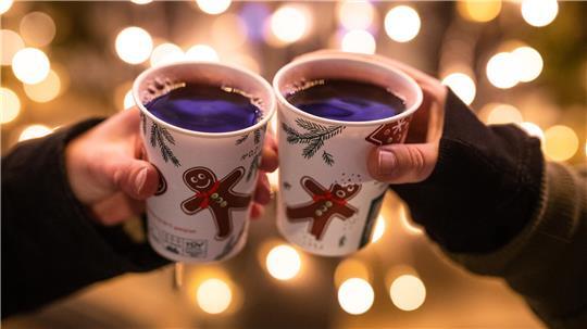 Zwei Frauen stoßen mit Glühwein gefüllten Bechern auf dem Weihnachtsmarkt an.