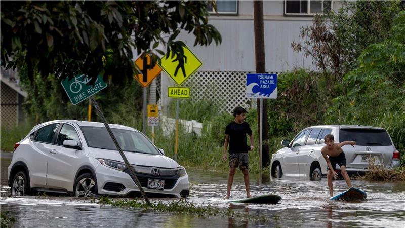 Zwei Jugendliche surfen in Waialua neben einem liegengebliebenen Fahrzeug im Hochwasser.