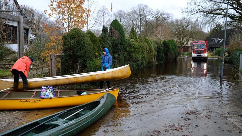 Zwei Jugendliche tragen ein Kanu an einer überfluteten Straße in Borgfeld bei Bremen.