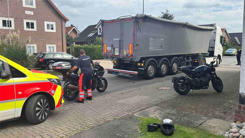 Ein Mann richtet ein Motorrad auf. Ein Lkw, ein weiteres Motorrad und ein Rettungswagen sind im Bild zu sehen.