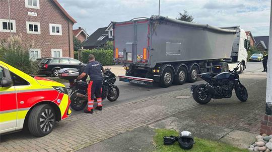 Ein Mann richtet ein Motorrad auf. Ein Lkw, ein weiteres Motorrad und ein Rettungswagen sind im Bild zu sehen.