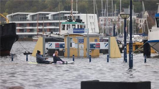 Zwei Personen paddeln auf einem Stand-Up-Padle Board über das Wasser am Hafen.