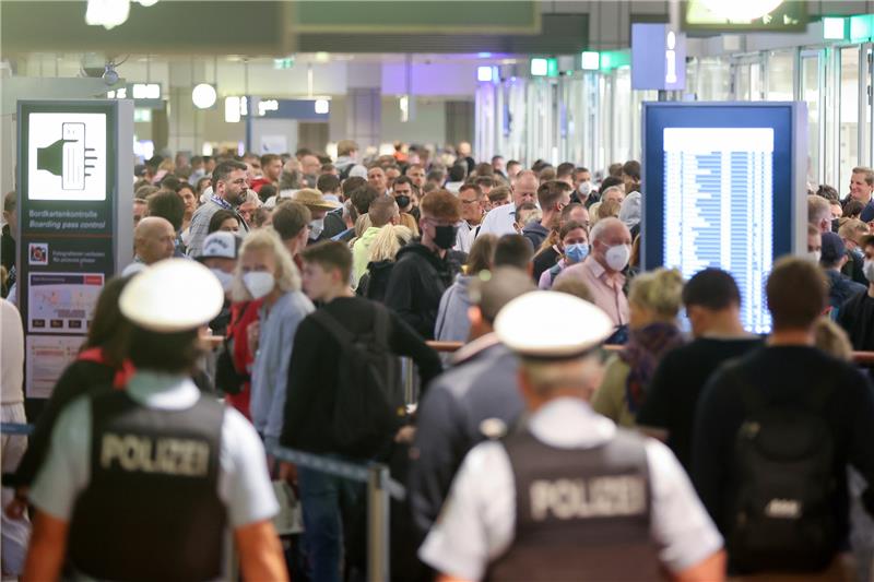 Zwei Polizisten beobachten im Sommer 2022 wie zahlreiche Reisende in Schlangen an der Sicherheitskontrolle am Hamburger Flughafen stehen. Foto: Bodo Marks/dpa