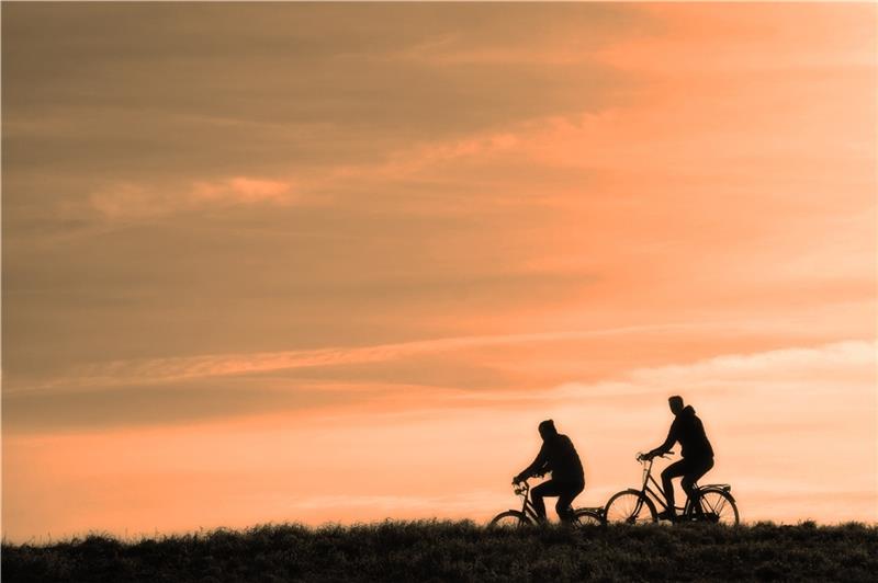 Zwei Raderfahrer fahren im Sonnenuntergang. Es ist nur ihre Silhouette zu sehen. Foto: pixabay