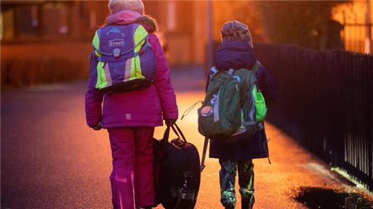 Zwei Schüler gehen am frühen Morgen auf dem Schulweg zu ihrer Grundschule in der Region Hannover.
