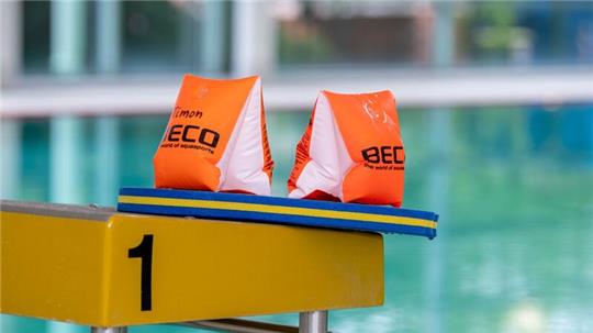 Zwei Schwimmflügel und ein Schwimmbrett liegen auf einem Startblock in der Schwimmhalle des Moskaubads.